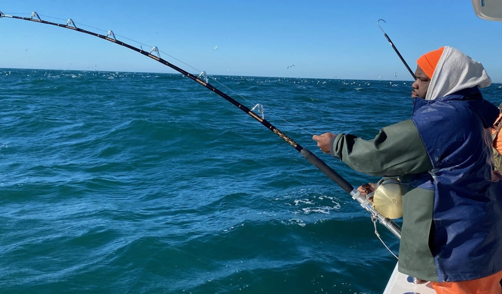 Person uses fishing pole to fish in ocean from a boat.