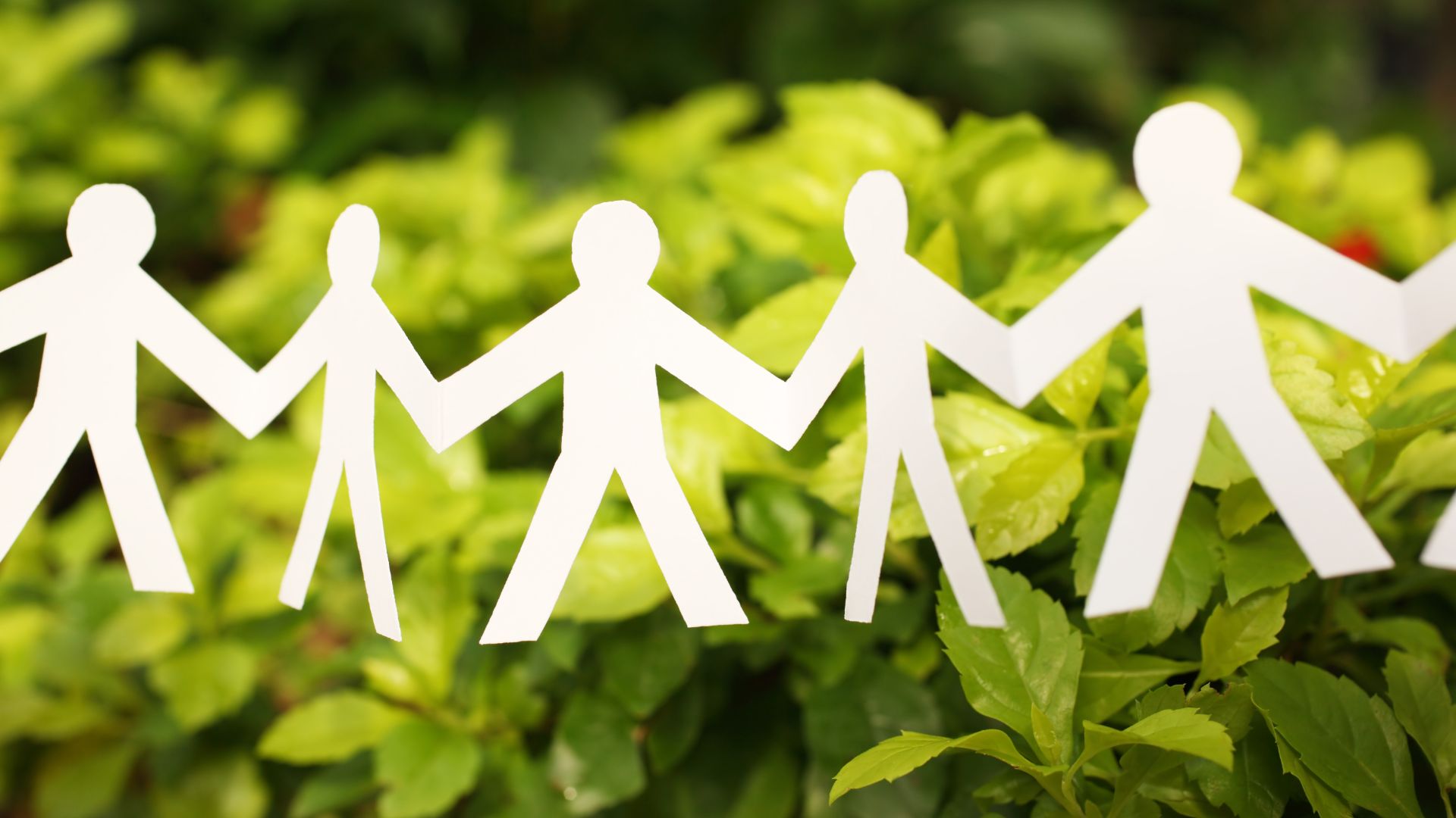 Paper cutout of people joining hands in front of a green leaf background.